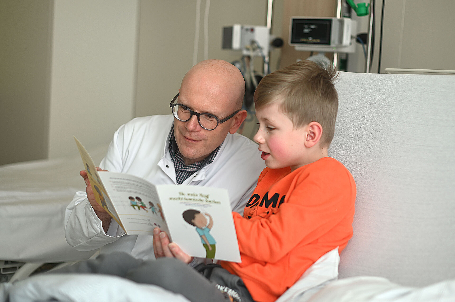 Ein Arzt schaut zusammen mit einem kleinen Jungen gespannt in ein Kinderbuch.