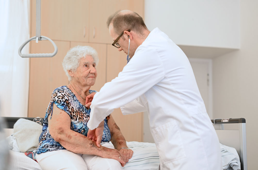 Ein Arzt untersuch eine ältere Patientin die auf dem Patientenbett sitzt