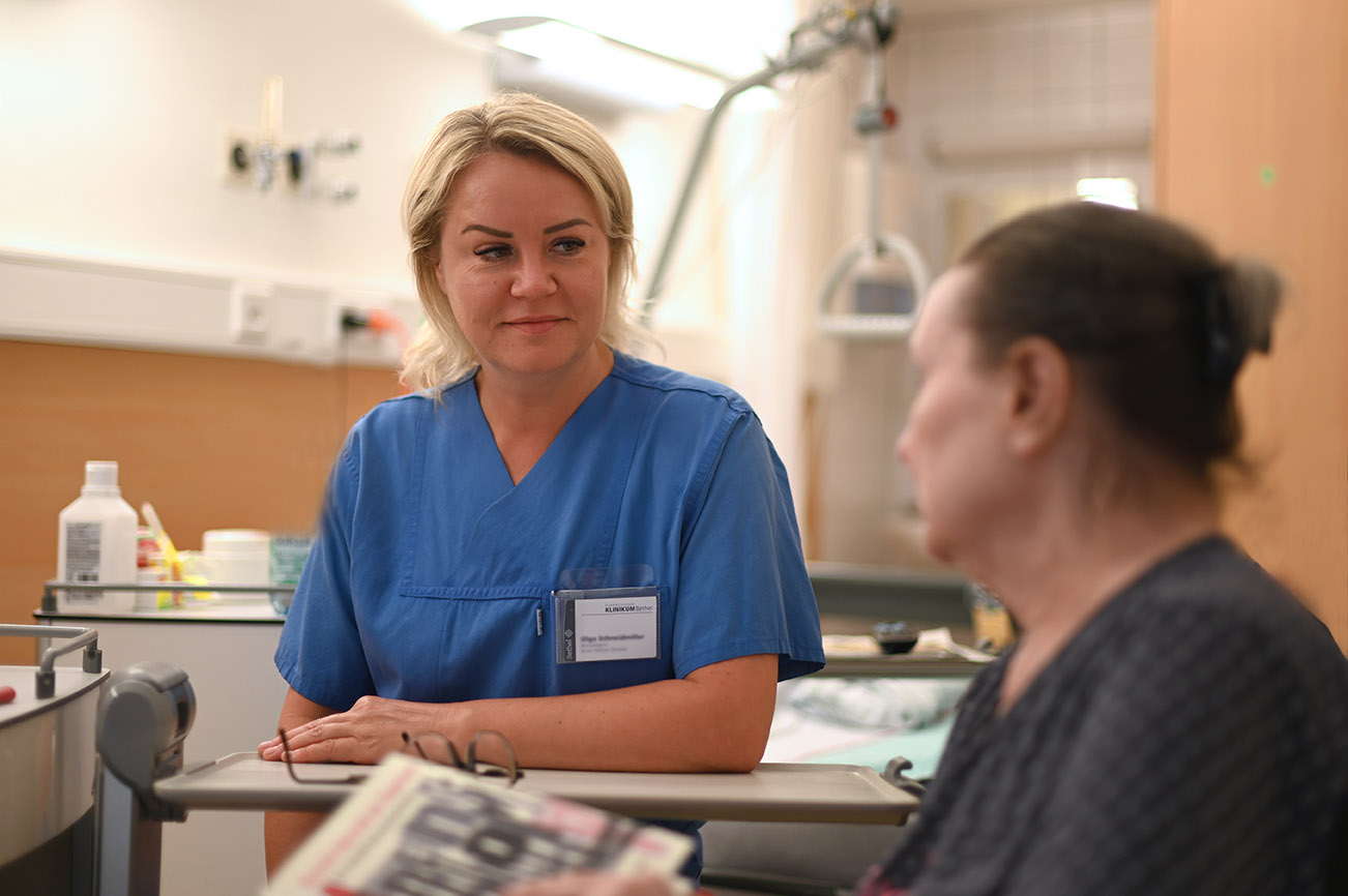 Gespräch zwischen Pflegekraft und Patientin im Patientenzimmer.
