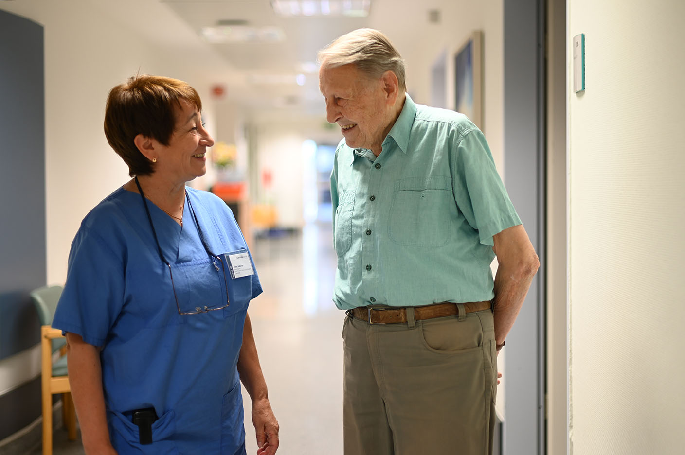 Eine weibliche Pflegekraft unterhält sich auf dem Flur mit einem Patienten.