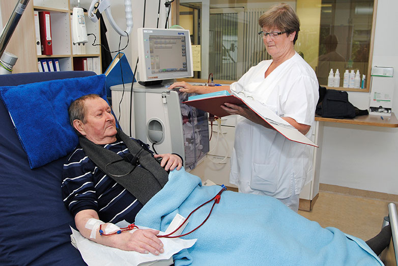 Ein Mann bei der Dialyse. Die Pflegekraft Kontrolliert alle Einstellungen am Dialysegerät.